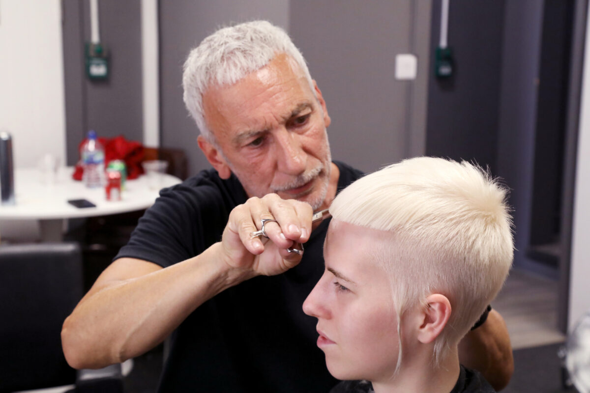 Hairdresser cutting a client’s platinum blonde pixie crop during a salon session.