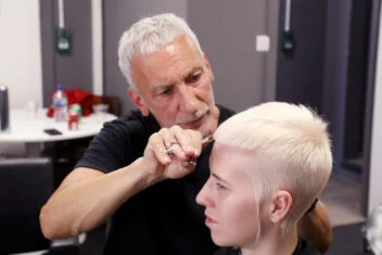 Hairdresser cutting a client’s platinum blonde pixie crop during a salon session.