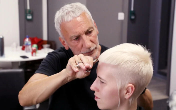 Hairdresser cutting a client’s platinum blonde pixie crop during a salon session.