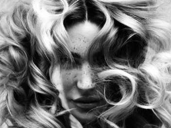 Black-and-white editorial portrait with voluminous curls framing the face and soft texture throughout the hair.