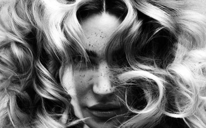Black-and-white editorial portrait with voluminous curls framing the face and soft texture throughout the hair.