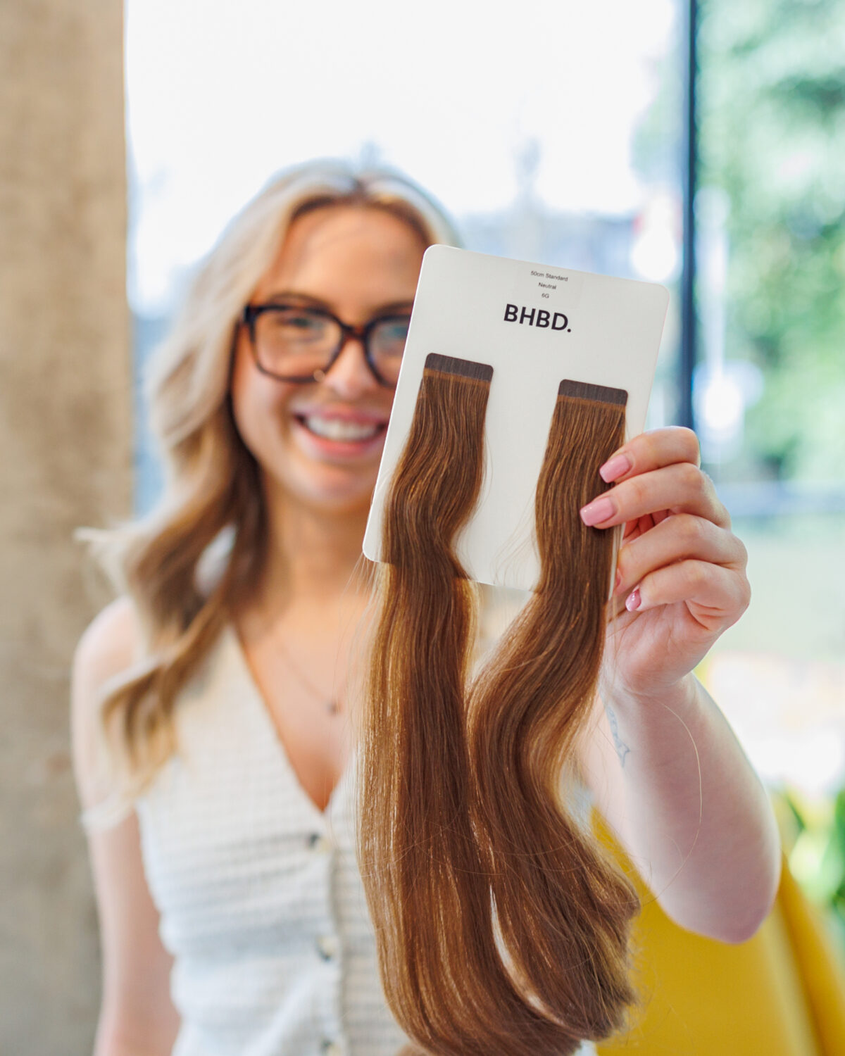 Woman holding a BHBD hair extension shade sample card during a salon training or consultation session.
